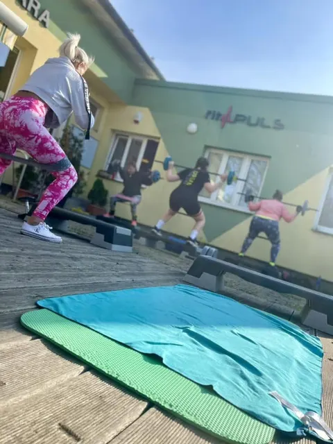 Cvičenky dělají dřepy s osou na terase před FitPULS