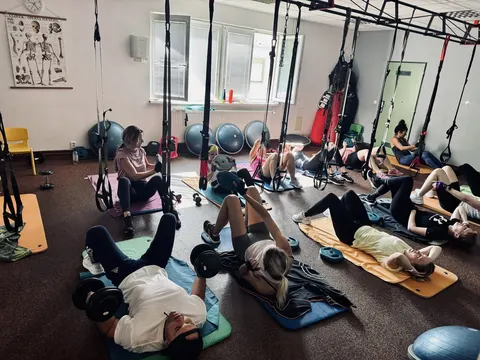 Cvičenci leží na podložkách s jednoručkami v sále s TRX