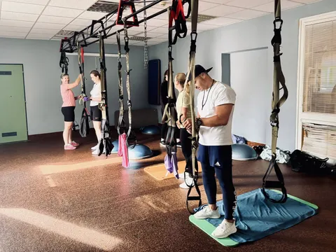 Trenér ukazuje cvičení v TRX popruzích skupině v sále