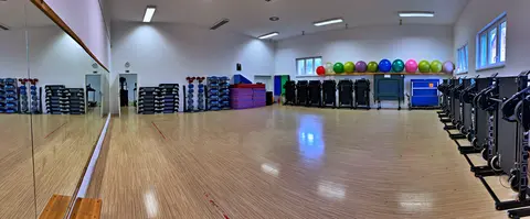 Prázdný sál se zrcadlovou stěnou, dřevěnou podlahou, stepy, míči a cvičebními pomůckami